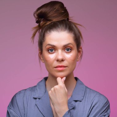 Göz bantları altında kadın yüzü resmi. Çenesine dokunan pembe pijama giymiş bir kadın..