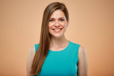 Şeftali rengi arka planda izole edilmiş yeşil masmavi elbiseli, gülümseyen kadın portresi