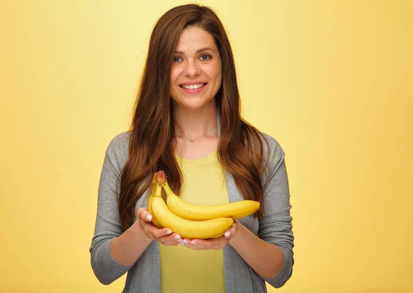 Happy woman holding bananas fruits isolated on yellow studio back. Smiling girl portrait.
