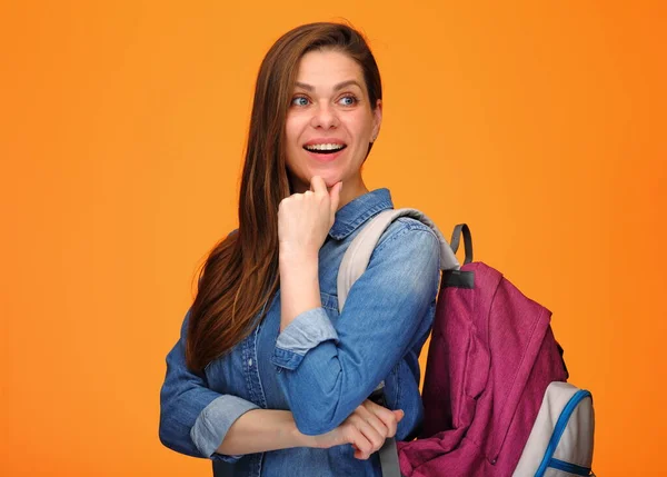 Woman student with backpack looking back over shoulder touching her chin. Idea and thinking posing on isolated orange back.