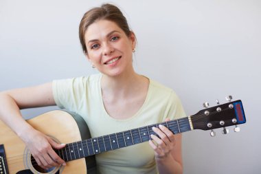Gülümseyen kadın gitarla oynar. Gri sırtlı izole edilmiş portre.
