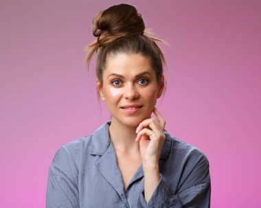 Göz altı bantlı, gülümseyen kadın çenesine dokunuyor, pembe kadın yüz portresi üzerinde çörekli saç stiliyle izole edilmiş..