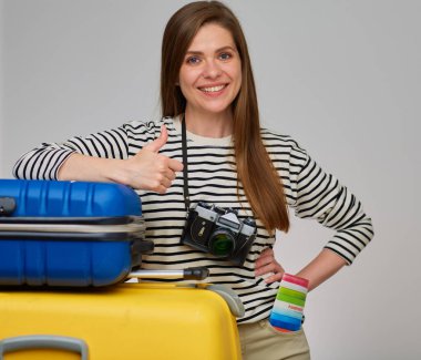 Seyahat çantası ve fotoğraf makinesiyle gülümseyen bir kadın için otostop çekmek. Parmağını kaldıran kız.