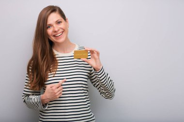 Elinde kredi kartıyla gülümseyen ve izole edilmiş bir portreyi işaret eden kadın. Uzun saçlı, çizgili sıradan gömlekli genç bir kadın..