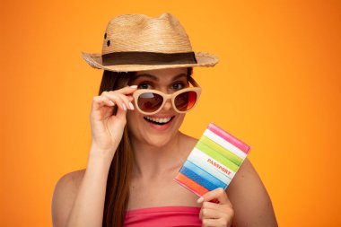 Meksika şapkalı gülümseyen kadın elinde pasaportuyla güneş gözlüğüne dokunuyor. yalıtılmış yüz portresi çıplak omuzlu turuncu sarı arka plan.