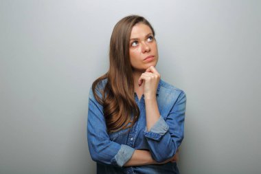 Mavi günlük kot gömlekli ciddi bir kadın düşünüyor, yukarı bakıyor. soyutlanmış kadın portresi.