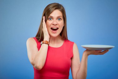 Kırmızı elbiseli, elinde boş tabakla şaşırtıcı bir kadın. Mavi arka planda izole edilmiş kadın portresi.