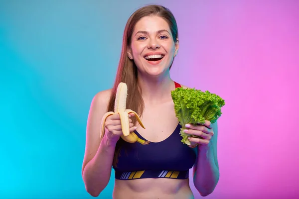 サラダ束とバナナを持った笑顔の幸せな女性 健康食品とネオンカラーの背景に隔離された女性のフィットネスの肖像画 — ストック写真