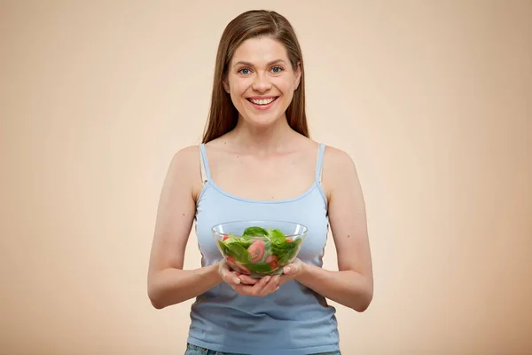 面带微笑的女人把绿色沙拉放在碗里 把孤立的肖像放在米黄色的背上 — 图库照片