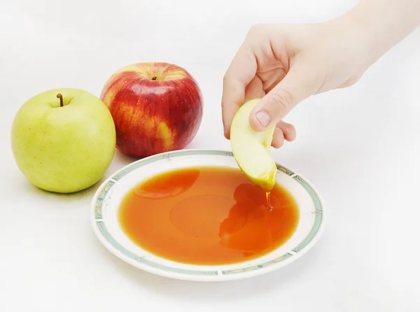 Mano sumergiendo el pedazo de manzana en la miel como sym año nuevo judío —  Fotos de Stock