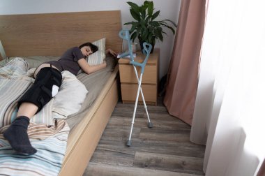 ACL ameliyatı olan bir kadın yakınlarda koltuk değnekleriyle evde uyuyor..