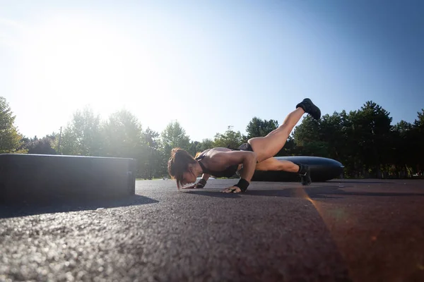 Young fitness woman doing push ups with one leg up in the park.