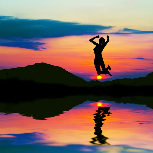 Silhouette einer glücklichen Frau, die bei Sonnenuntergang springt — Stockfoto