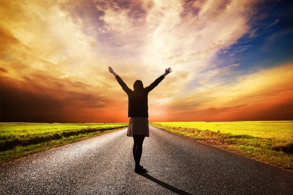 Happy woman standing on long road at sunset — Stock Photo, Image