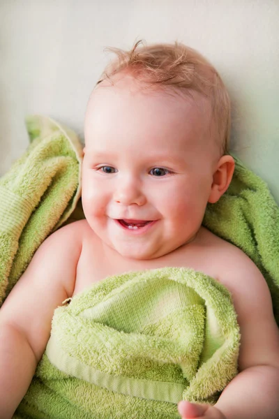 Ein glückliches Baby im grünen Handtuch auf dem Bett liegend — Stockfoto