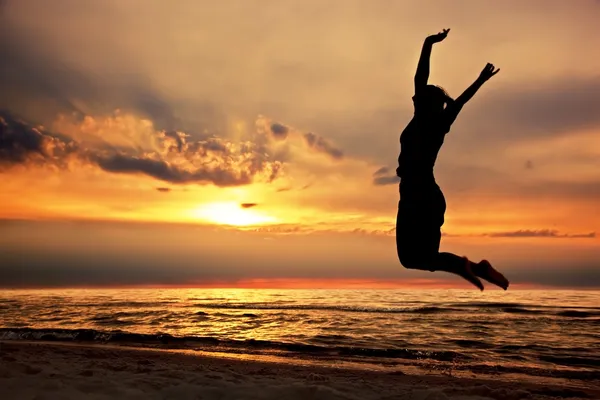 Glückliche Frau springt bei Sonnenuntergang an den Strand — Stockfoto