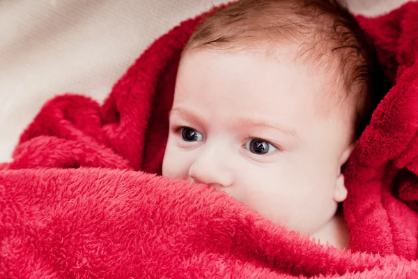 Маленький трехмесячный ребенок лежит на кровати, покрытой красным одеялом . — стоковое фото