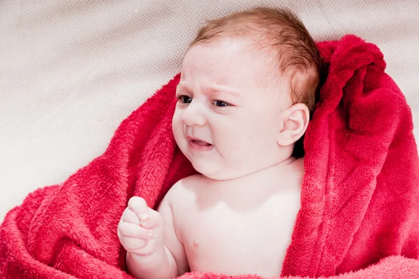 A 3 months baby crying while lying on bed covered with red blanket. — Stock Photo, Image