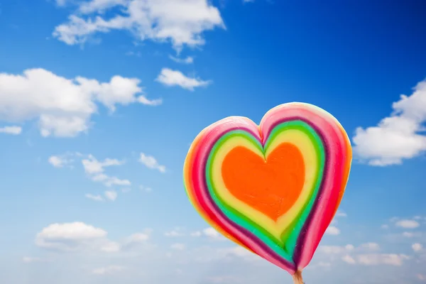 Kleurrijke hartvormige lollipop op hemelachtergrond — Stockfoto