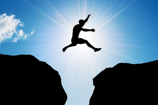 Man jumping over precipice between two rocky mountains — Stock Photo, Image