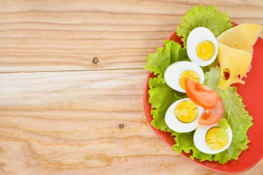 Kahvaltı arka plan. Katı pişmiş yumurta, dilimlenmiş yarım, salata, domates ve peynir kırmızı plaka ve ahşap zemin üzerinde yapılan.