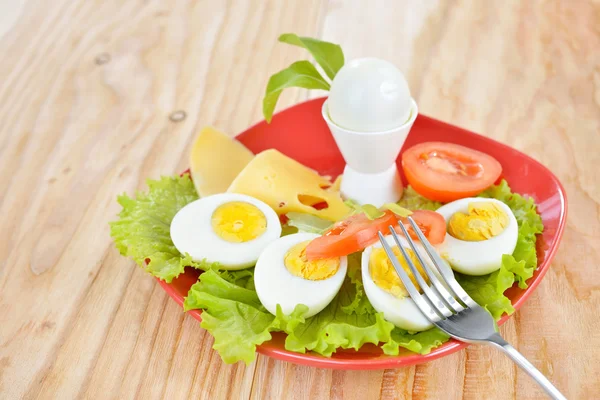 Frühstück mit hartgekochten Eiern, halbiert, Salat, Tomaten, Käse und Brot auf dem roten Teller und Holzboden — Stockfoto