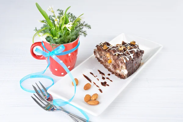 Still life with cake and flowers. Piece of tasty chocolate cake with black chocolate sauce