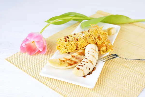 Крупним планом зображення смачних млинців з бананом і шоколадним сиропом на ньому. Красива квітка тюльпанів на фоні . — стокове фото