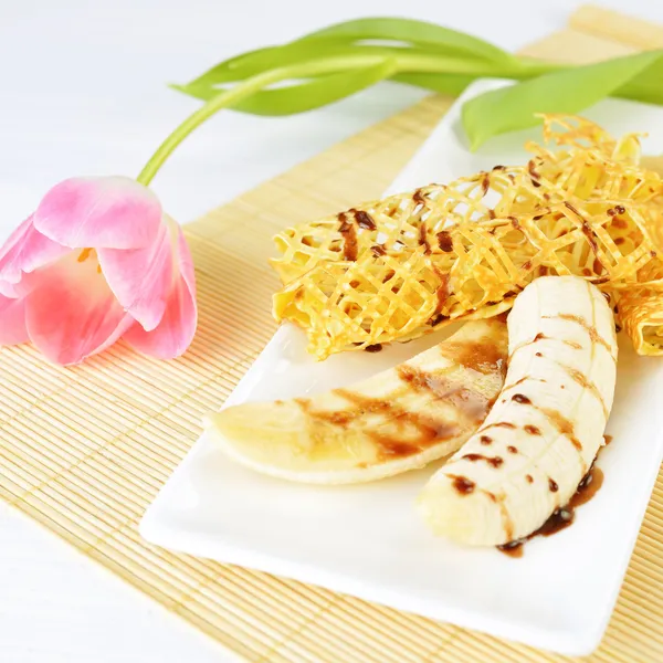 Imagen de primer plano de una deliciosa tortitas con plátano y jarabe de chocolate en ella. Hermosa flor de tulipán en el fondo . — Foto de Stock