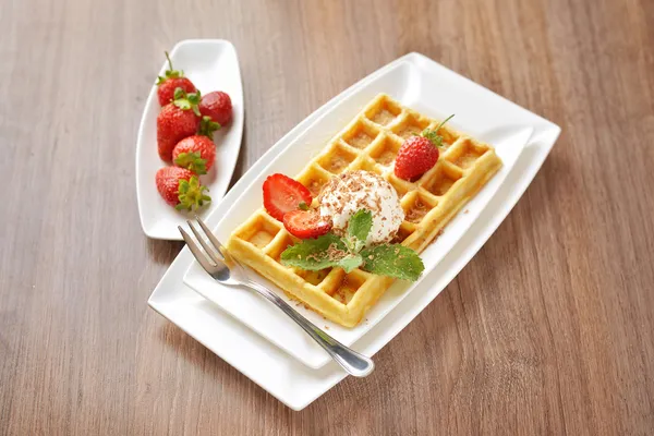 Frühstücksdessert - goldene Waffeln mit Eis und frisch geschnittenen Erdbeeren mit Zucker und Schokolade bestreut lizenzfreie Stockfotos