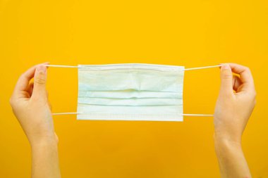 Sarı arka planda tıbbi koruyucu maske tutan bir el. Virüs koruması. Bir salgın..