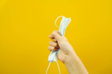 Sarı arka planda tıbbi koruyucu maske tutan bir el. Virüs koruması. Bir salgın..