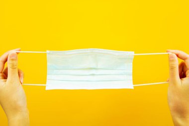 Sarı arka planda tıbbi koruyucu maske tutan bir el. Virüs koruması. Bir salgın..