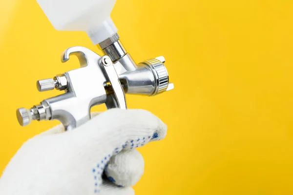 Manual and paint spray gun at work on a yellow background — Stockfoto