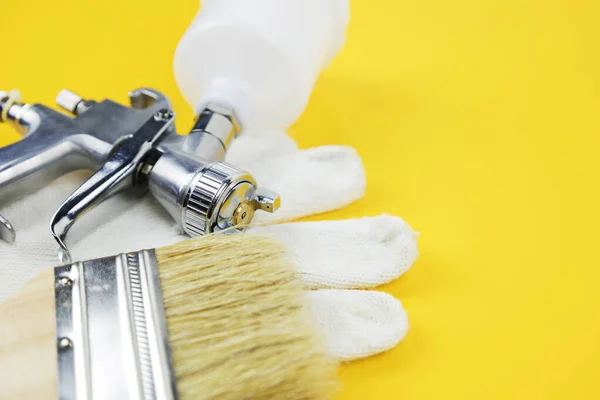 Brush, gloves and spray gun on yellow background — стоковое фото