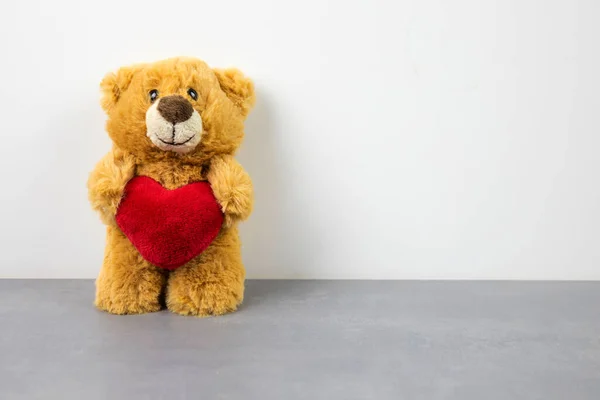 A teddy bear doll holding a heart-shaped pillow with love. — Stock Photo, Image