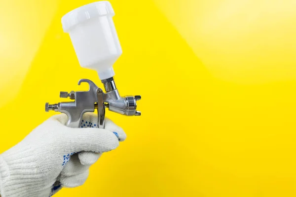 Manual and paint spray gun at work on a yellow background — Stockfoto