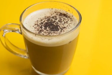 Sütlü güzel kahve köpüğü. Sarı arka planda şeffaf bardakta sütlü kahve.