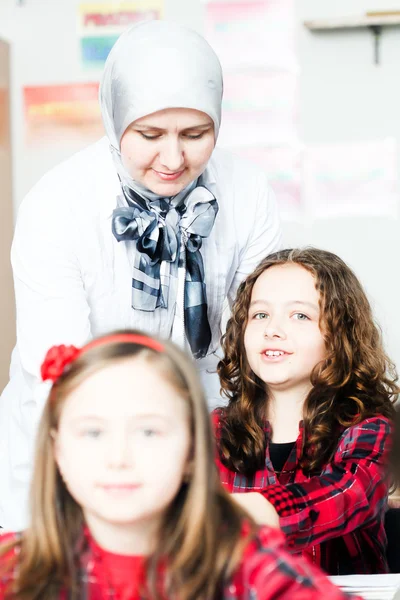 Two little schoolgirls with her young teacher in the classroom — Stock Photo, Image