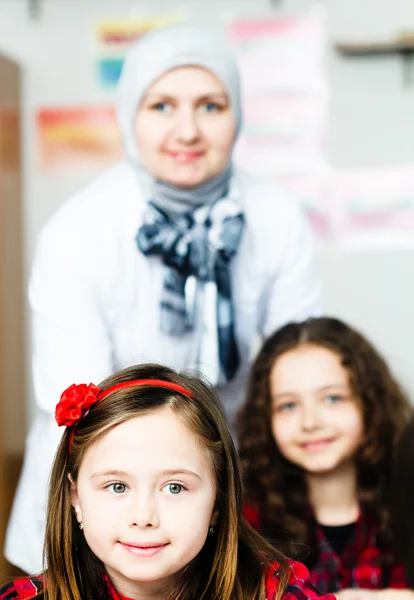 Deux petites écolières avec son jeune professeur en classe — Photo