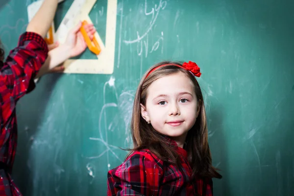 Menina bonita de pé na frente do quadro negro — Fotografia de Stock