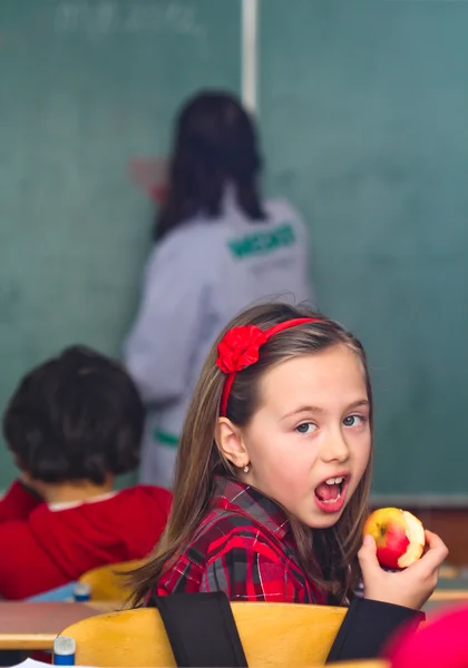 Счастливая маленькая школьница с яблоком - портрет в классе — стоковое фото