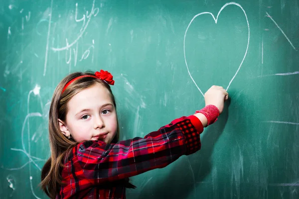 Hübsches kleines Mädchen zeichnet Herz auf Tafel Stockbild
