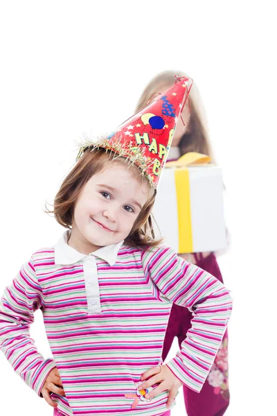 Little girl with birthday hat and her sister with gift in backgr — Stock Photo, Image