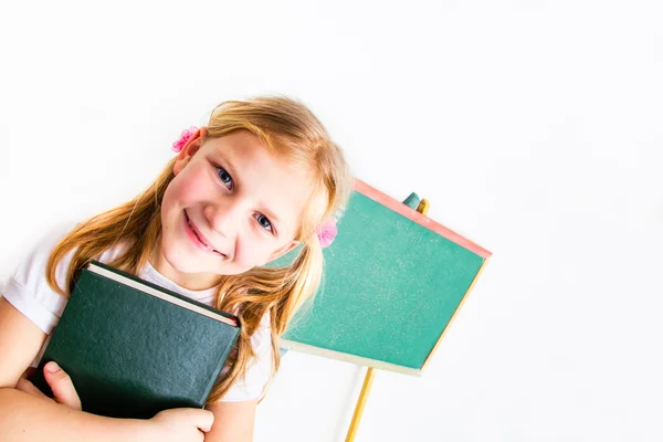 Pequeña colegiala sosteniendo un libro y de pie frente a la negrura — Foto de Stock