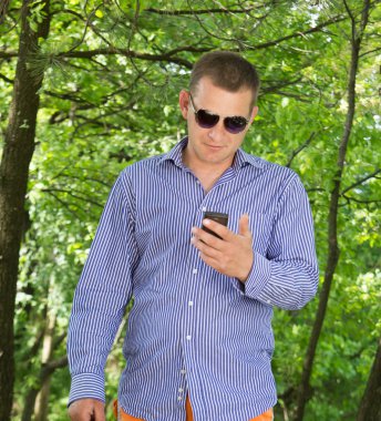 Yeşil ormanda yürürken telefon kullanan genç adam