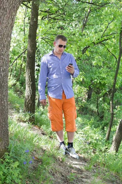 Młody człowiek przy użyciu telefonu podczas spaceru przez zielony las — Zdjęcie stockowe