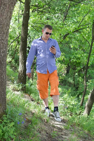 Jovem usando telefone enquanto caminha pela floresta verde — Fotografia de Stock