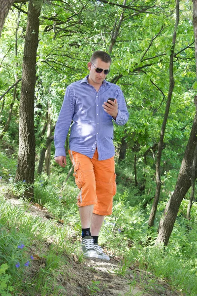 Junger Mann telefoniert beim Spaziergang durch den grünen Wald — Stockfoto