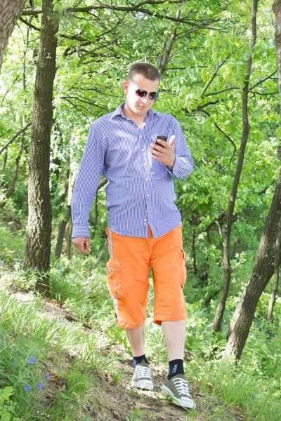 젊은 남자는 녹색 숲을 걷는 동안 전화를 사용 하 여 — 스톡 사진